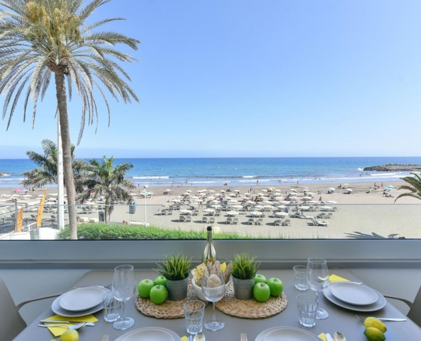 Tavolo apparecchiato in appartamento workation con vista sull'oceano e spiaggia a Gran Canaria, con palme e ombrelloni.